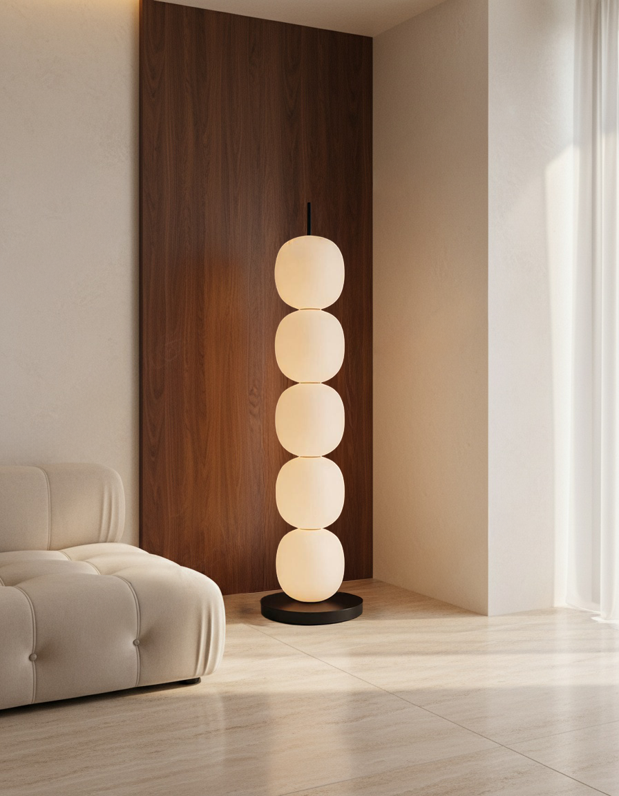 Five-globe sculptural floor lamp in warm white glass and black metal base, standing beside a beige sofa and walnut wall panel in a minimalist Scandinavian interior with natural daylight.